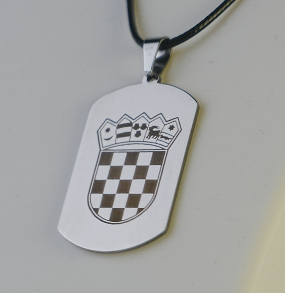 Metallic dog tag with a checkered design and emblem on a light gray background