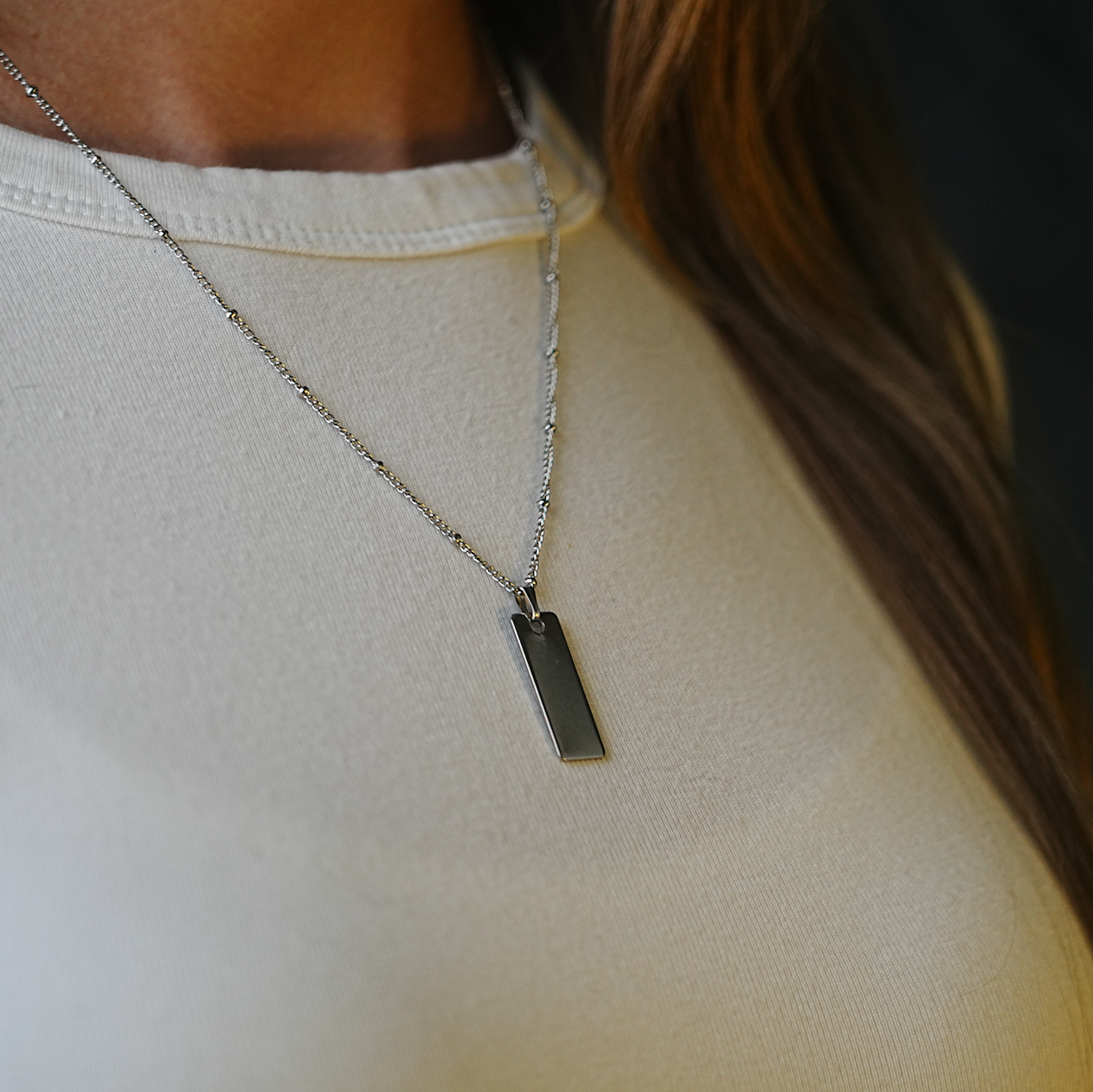 Necklace with a rectangular pendant on a person wearing a white top.