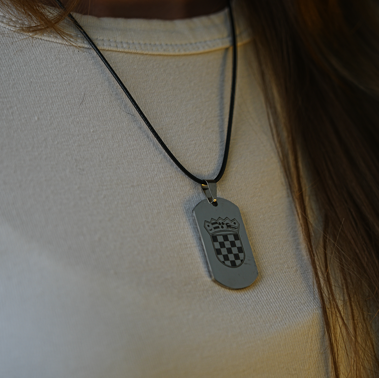 Necklace with a silver dog tag featuring a crest design on a white shirt.