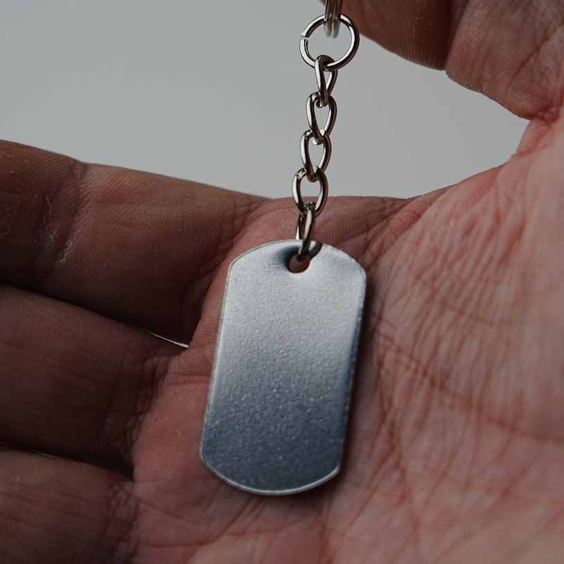 Hand holding a silver dog tag keychain against a neutral background