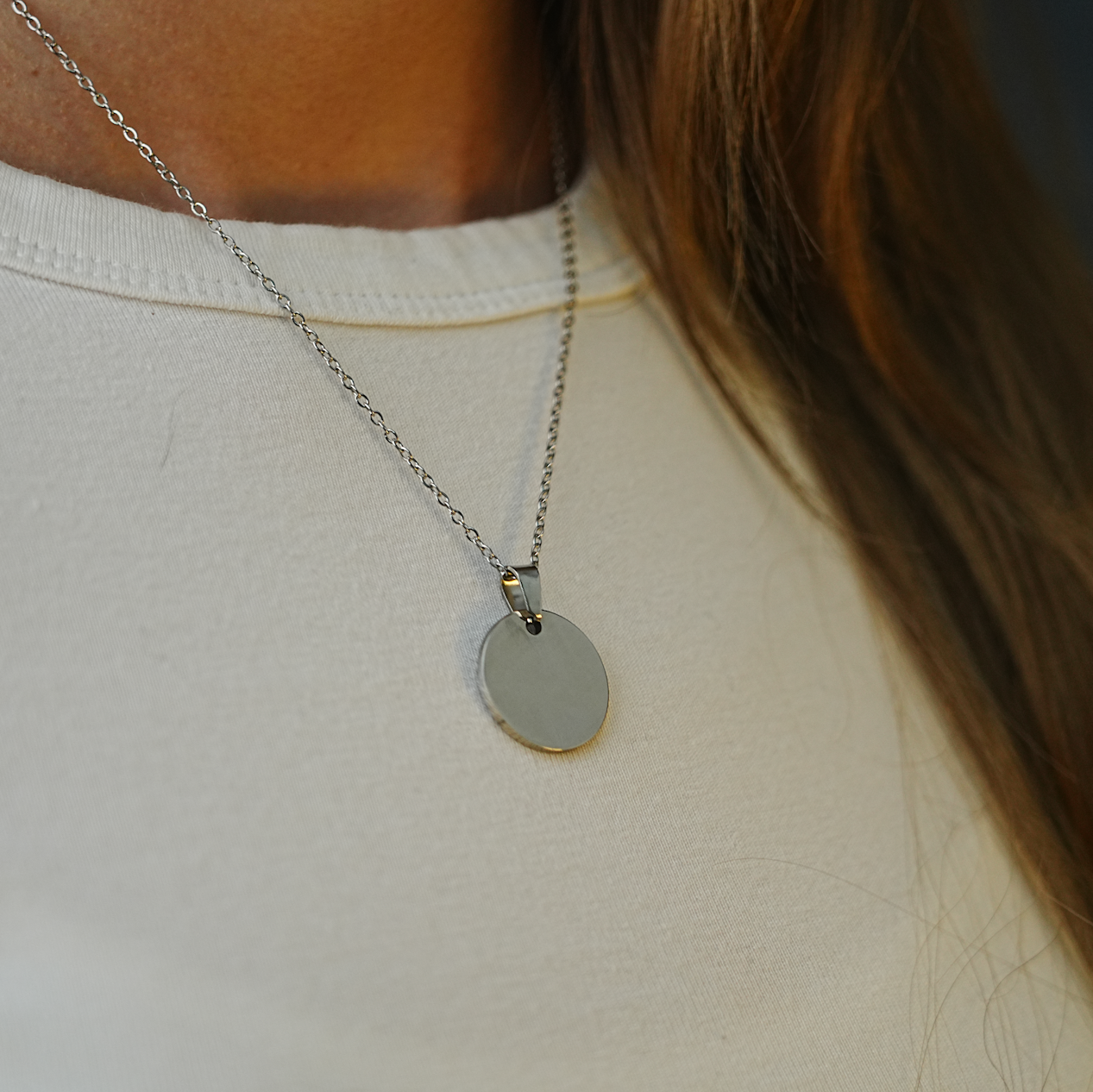 Necklace with a round pendant on a person wearing a white top.